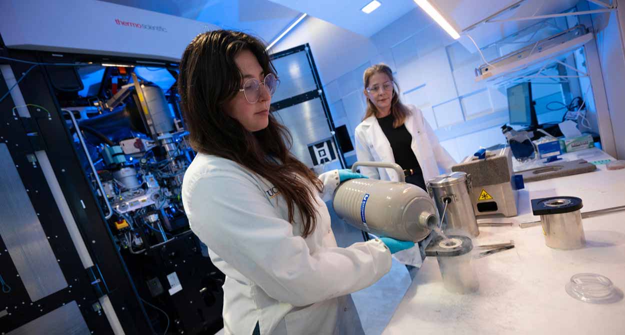 Student handles lab equipment while another lab member observes